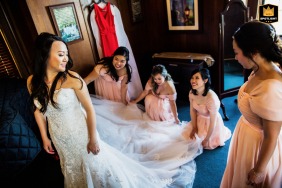 At the historic Kohl Mansion in Burlingame, CA, the bridesmaids work together in a "getting ready" moment, carefully fanning out the bride's wedding dress.